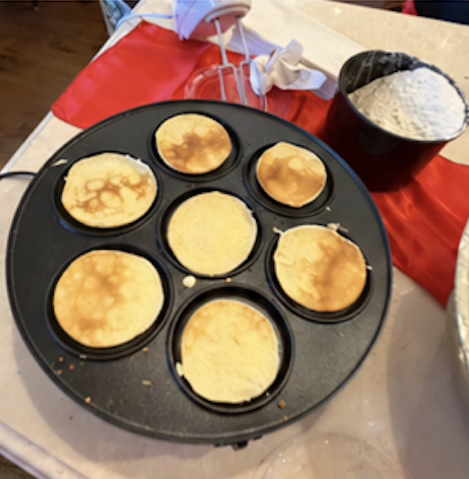Crêpes cooking on a round griddle beside a bowl of batter.