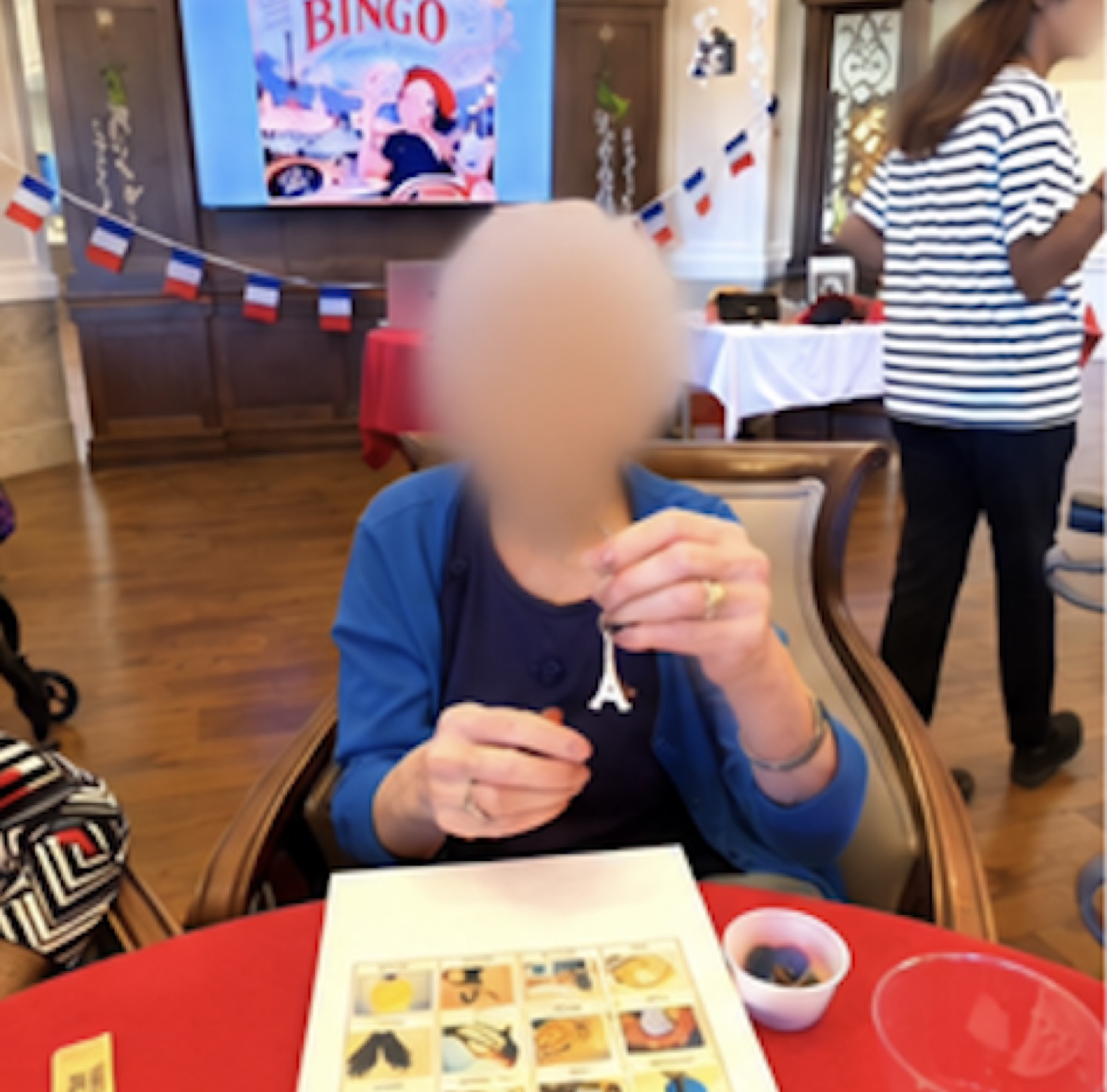 A resident holding a small Eiffel Tower charm at a French Salon table.