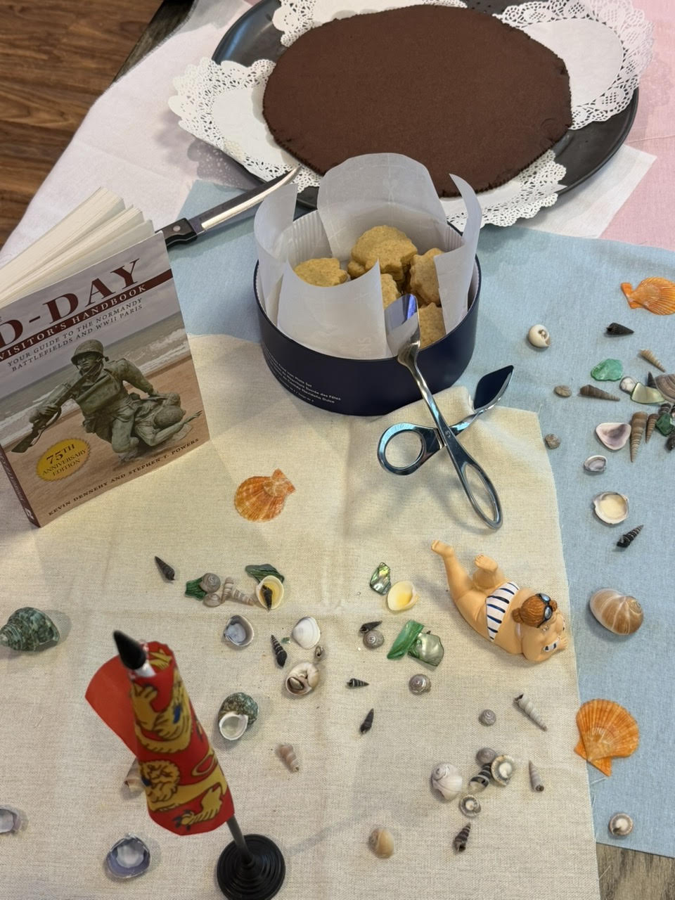 Shells, sea glass, shortbread, and a Normandy guidebook laid out for a French Salon session.
